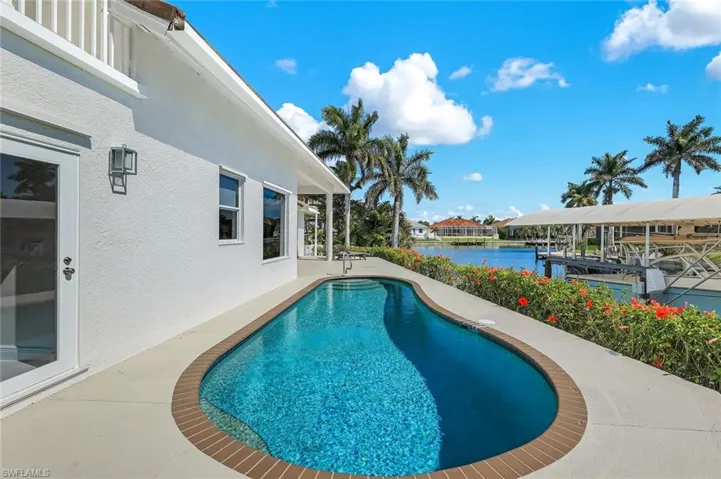Outdoor pool with a water view, a patio area, a dock, and boat lift