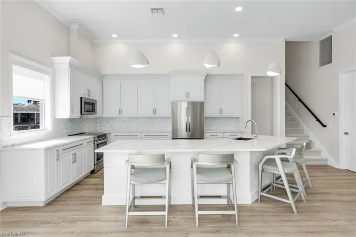 Kitchen with stainless steel appliances, a kitchen bar, a spacious island, tasteful backsplash, and white cabinets