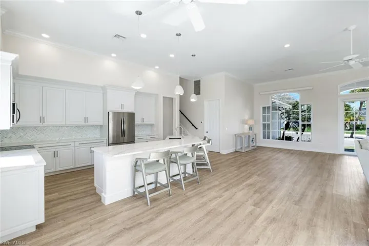 Kitchen with a ceiling fan, light stone counters, stainless steel appliances, tasteful backsplash, and white cabinetry