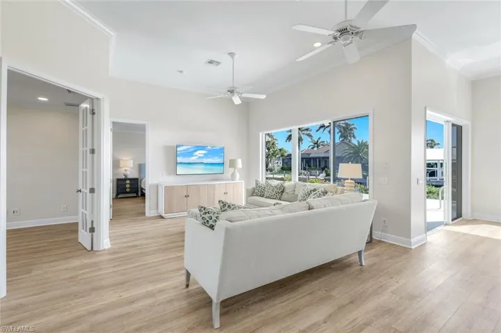 Living area with a ceiling fan, light wood-type flooring, recessed lighting, crown molding, and a high ceiling