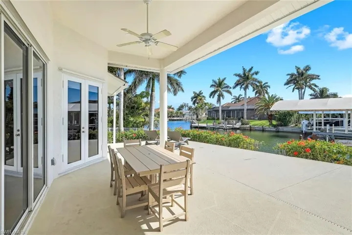 View of patio featuring french doors, a water view, outdoor dining space, a ceiling fan, and a dock