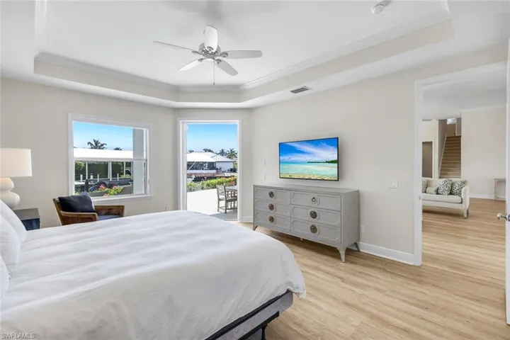 Bedroom with access to outside, crown molding, light wood-style flooring, a raised ceiling, and ceiling fan