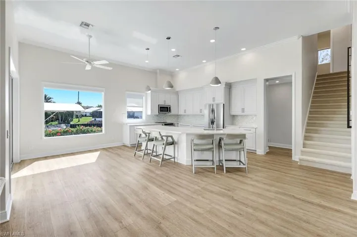 Kitchen with a kitchen island with sink, a breakfast bar, white cabinets, stainless steel appliances, and a ceiling fan