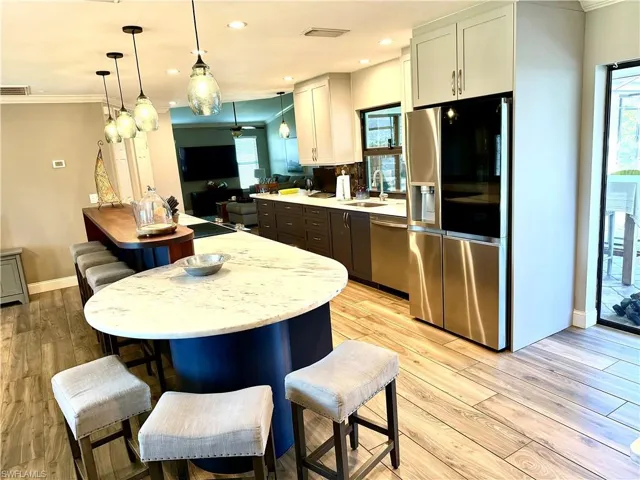 Kitchen with stainless steel appliances, crown molding, decorative light fixtures, light wood finished floors, and a breakfast bar