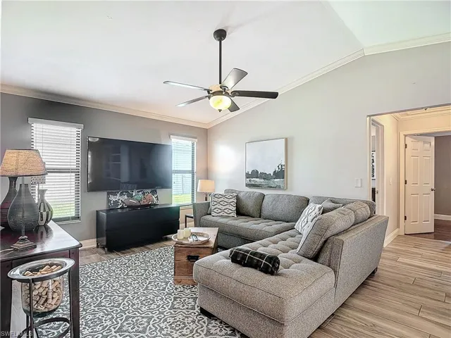 Living room featuring crown molding, lofted ceiling, light wood-style flooring, and a ceiling fan