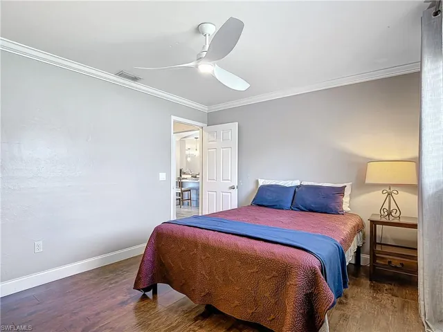 Bedroom with ornamental molding, dark wood-type flooring, and ceiling fan
