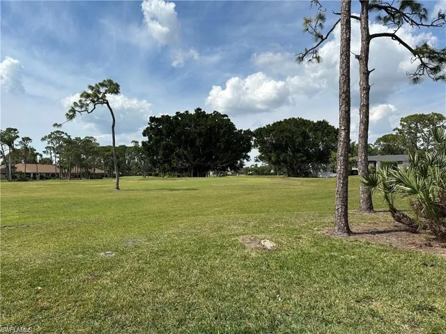 Expansive green space featuring mature trees and distant residential structures