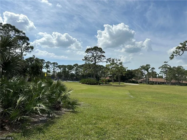 Expansive green golf course featuring manicured fairways, mature palm trees, and distant residential structures