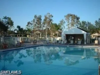Outdoor swimming pool with a surrounding fence, poolside cabana, and mature trees