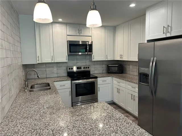 Contemporary kitchen featuring white cabinetry, granite-finish countertops, stainless steel appliances, and a tiled backsplash