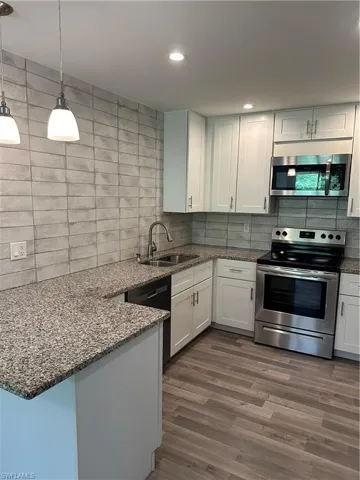 Kitchen featuring granite countertops, white cabinetry, stainless steel appliances, wood-finish flooring, and pendant lighting