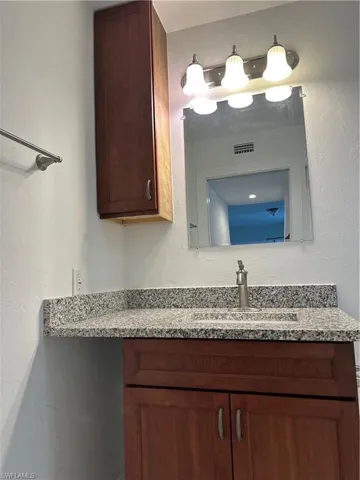 Vanity with cherry wood-finish cabinetry and a granite countertop featuring an undermount sink