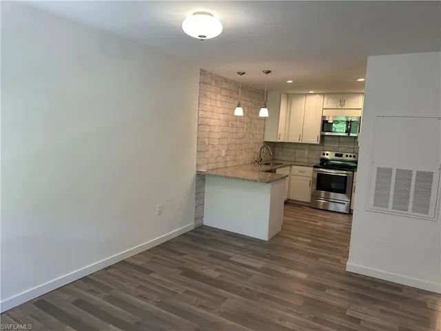 Spacious open-concept area featuring wood-finish flooring, a kitchen with stainless steel appliances, white cabinetry, and a peninsula with a stone countertop