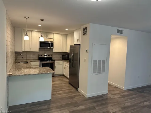 Kitchen featuring white cabinetry, stone-finish countertops, stainless steel appliances, and wood-look flooring