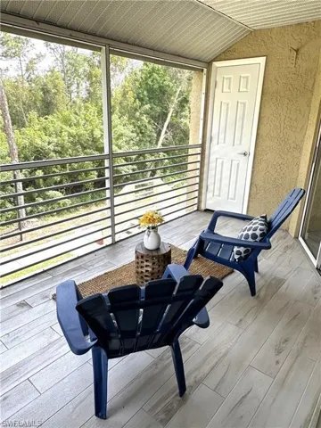 Screened balcony featuring wood-finish flooring, textured exterior wall, a white panel door, and a horizontal bar railing