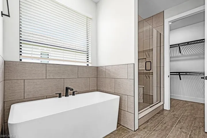 Bathroom featuring a freestanding bath, a shower stall, a spacious closet, and tile walls