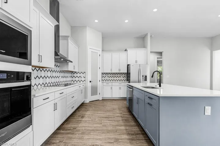 Kitchen featuring white cabinetry, appliances with stainless steel finishes, light wood-style flooring, light stone counters, and a kitchen island with sink