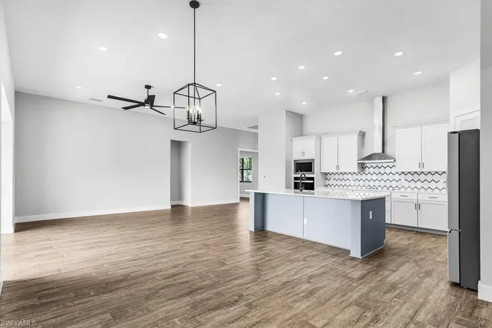 Kitchen with pendant lighting, a kitchen island with sink, white cabinets, a chandelier, and open floor plan