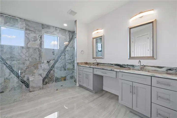 Full bath featuring a marble finish shower, double vanity, healthy amount of natural light, and recessed lighting