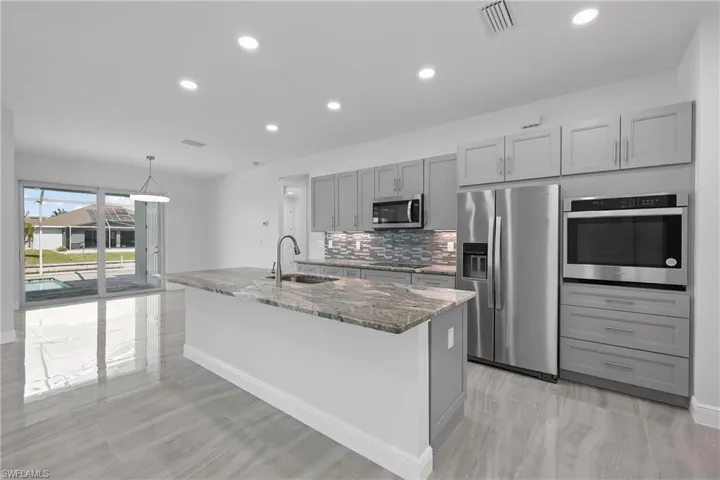 Kitchen featuring gray cabinets, light stone counters, appliances with stainless steel finishes, tasteful backsplash, and a center island with sink