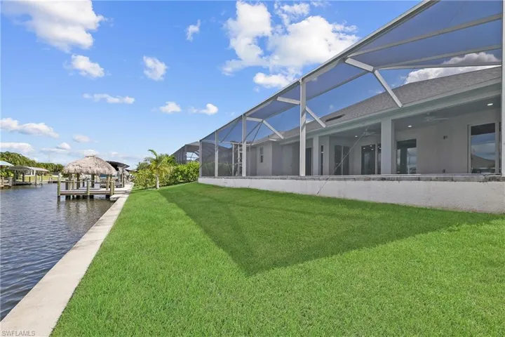 View of green lawn featuring a lanai, a sunroom, a patio, ceiling fan, and a boat dock