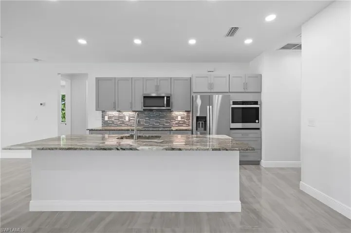 Kitchen with gray cabinets, dark stone counters, tasteful backsplash, appliances with stainless steel finishes, and recessed lighting