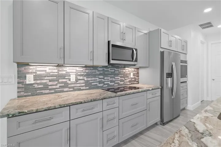 Kitchen featuring decorative backsplash, appliances with stainless steel finishes, gray cabinetry, light stone counters, and recessed lighting