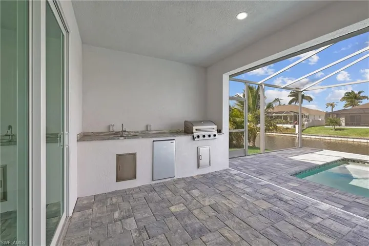 View of patio / terrace featuring glass enclosure, a sunroom, an outdoor kitchen, an outdoor pool, and a residential view