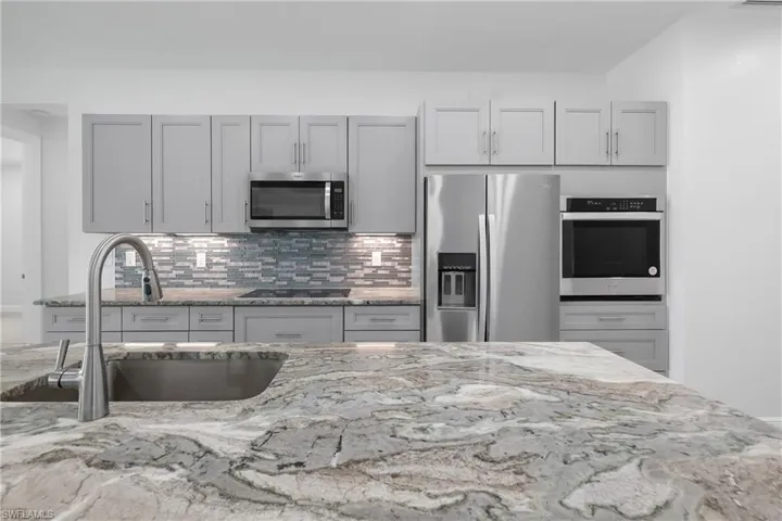 Kitchen featuring decorative backsplash, appliances with stainless steel finishes, light stone counters, and gray cabinets