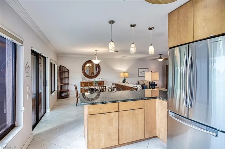 Kitchen with crown molding, light brown cabinets, stainless steel refrigerator, kitchen peninsula, and dark stone counters
