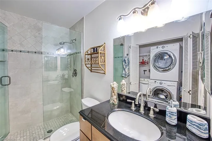 Bathroom featuring an enclosed Tile shower, vanity, toilet, and stacked washer and dryer