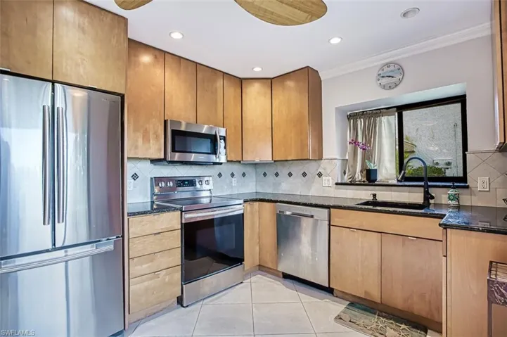Kitchen featuring sink, light tile patterned floors, dark stone countertops, stainless steel appliances, and ornamental molding