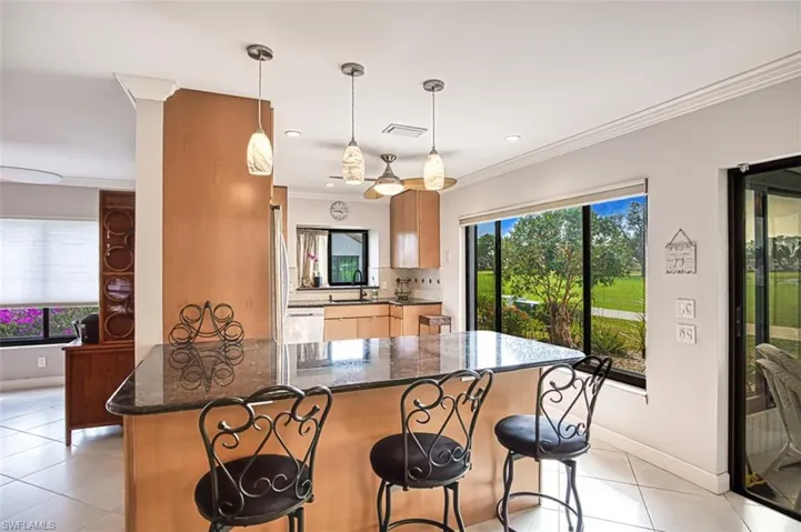 Kitchen with decorative light fixtures, sink, dark stone counters, ornamental molding, and light tile patterned floors