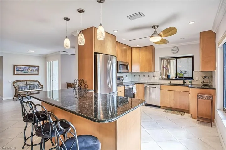Kitchen with stainless steel appliances, ornamental molding, hanging light fixtures, and dark stone countertops
