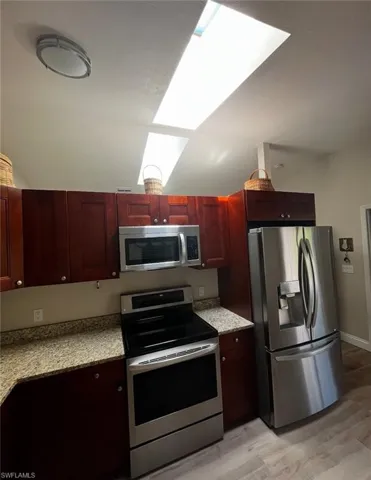 Kitchen featuring stainless steel appliances, dark brown cabinets, light wood-style flooring, a skylight, and lofted ceiling