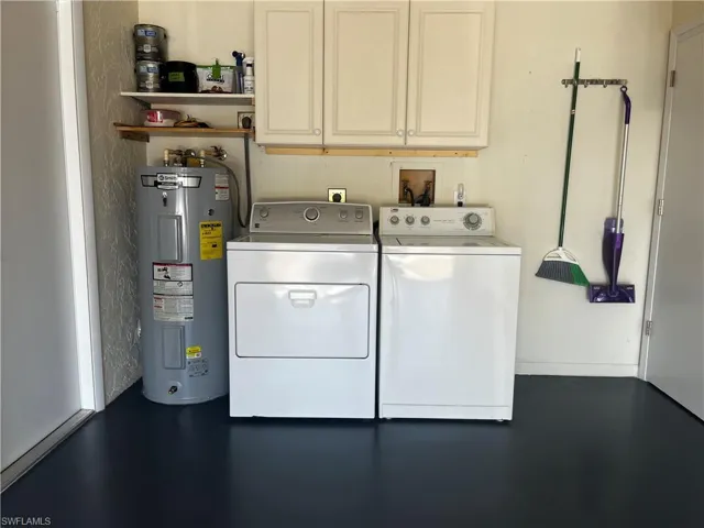 Clothes washing area featuring electric water heater, separate washer and dryer, and cabinet space