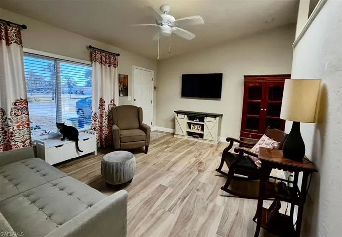 Living room with wood finished floors, a ceiling fan, lofted ceiling, and baseboards