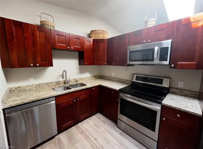 Kitchen with appliances with stainless steel finishes, reddish brown cabinets, a sink, light wood-style floors, and light stone counters