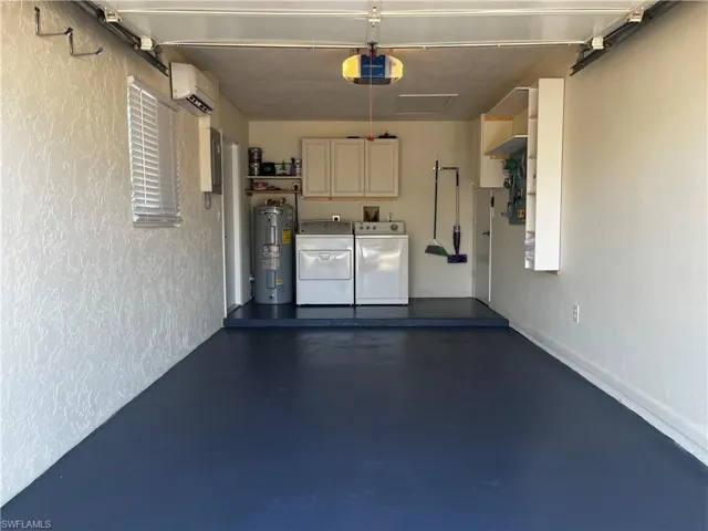 Garage with independent washer and dryer, electric water heater, a wall unit AC, and a garage door opener