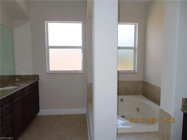 Bathroom with vanity, a tub with jets, and light tile patterned flooring