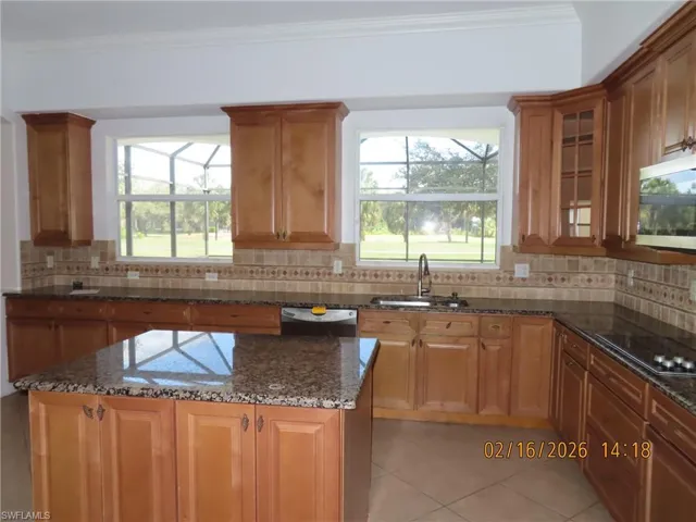 Kitchen with dark stone counters, stainless steel appliances, glass fronted cabinets, wood finish cabinetry, and crown molding