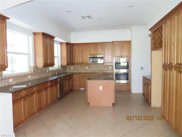 Kitchen with a kitchen island, dark stone countertops, stainless steel appliances, glass insert cabinets, and tasteful backsplash