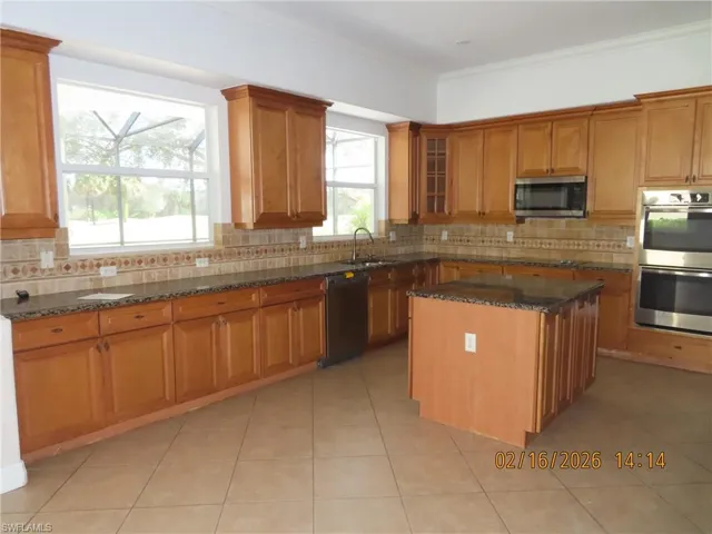 Kitchen with dark stone countertops, black appliances, wood finish cabinetry, glass insert cabinets, and light tile patterned floors