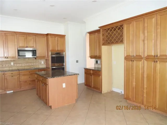 Kitchen featuring dark stone countertops, tasteful backsplash, stainless steel appliances, light tile patterned floors, and crown molding