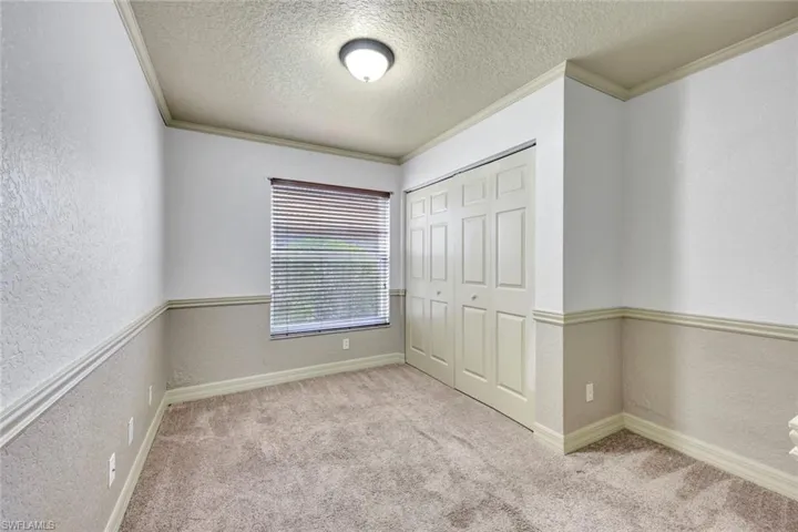 Unfurnished bedroom featuring a textured wall, crown molding, a textured ceiling, light colored carpet, and a closet
