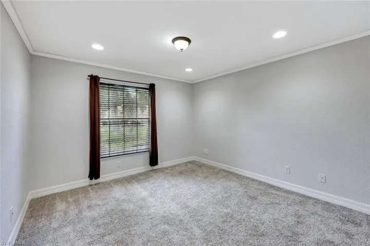 Empty room featuring light colored carpet, ornamental molding, a textured wall, and recessed lighting
