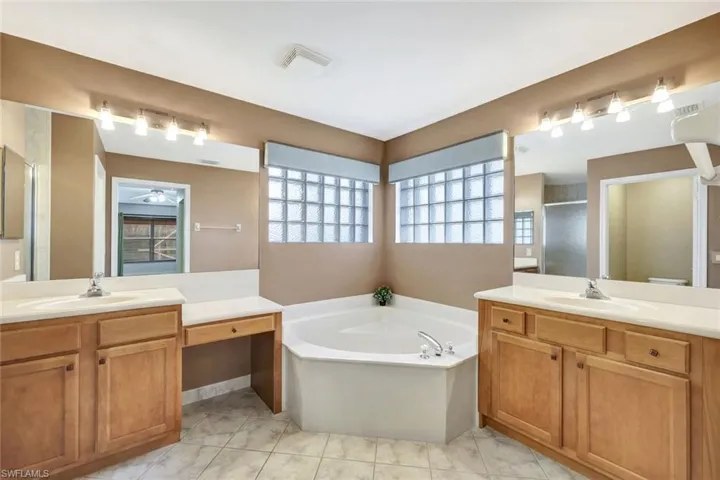 Full bath with two vanities, a shower stall, a bath, and light tile patterned floors