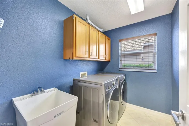 Laundry room featuring a textured wall, a textured ceiling, independent washer and dryer, cabinet space, and light tile patterned floors