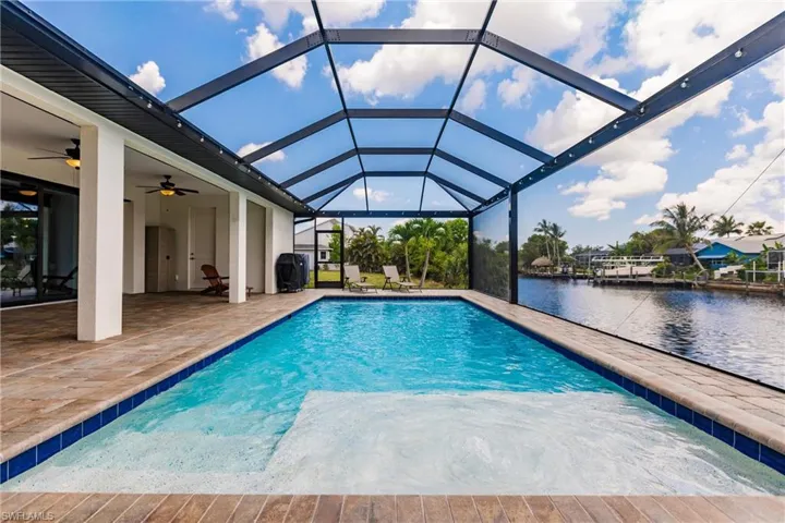 View of pool featuring ceiling fan, a water view, glass enclosure, and a patio area
