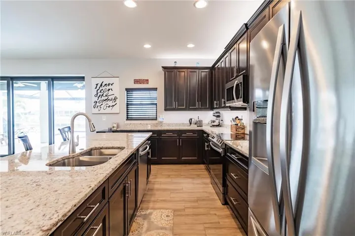 Kitchen with light stone countertops, dark brown cabinets, plank tile floors, sink, and appliances with stainless steel finishes
